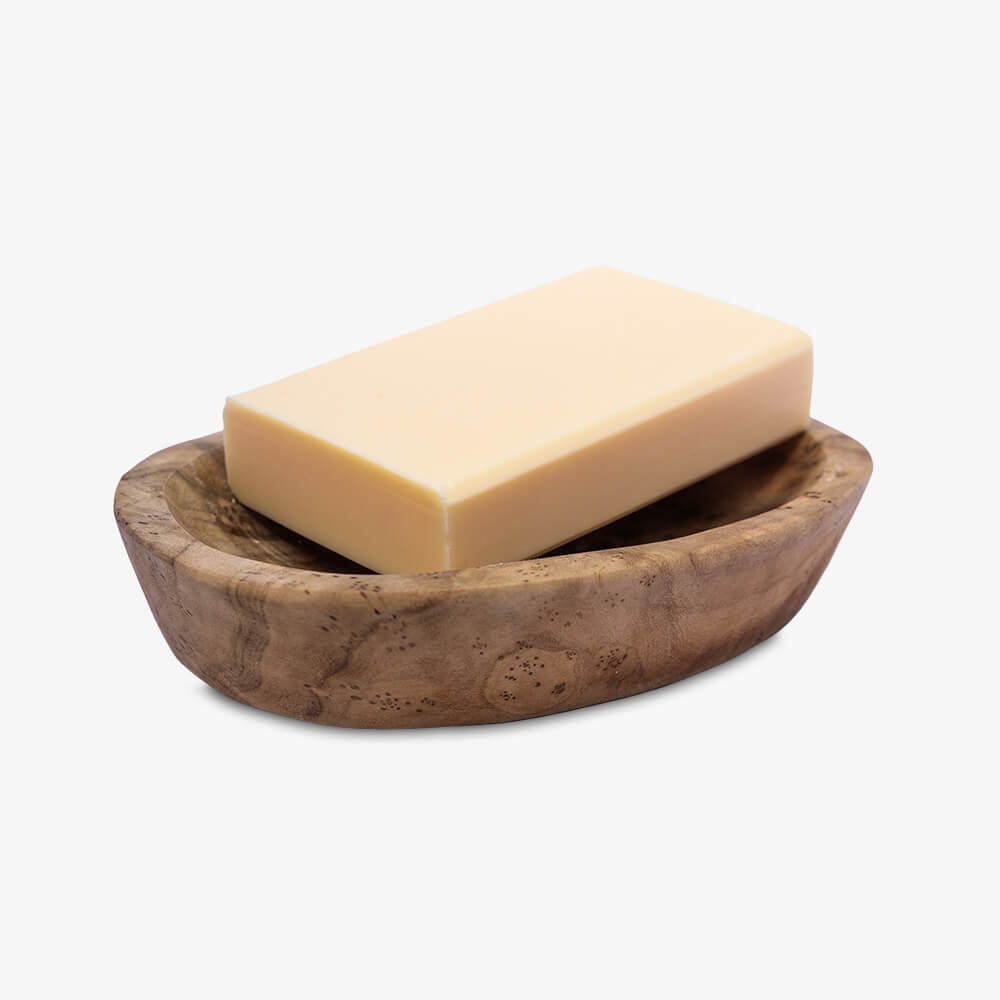 Hellgelbes Seifenstück liegt auf ovaler Holzschale