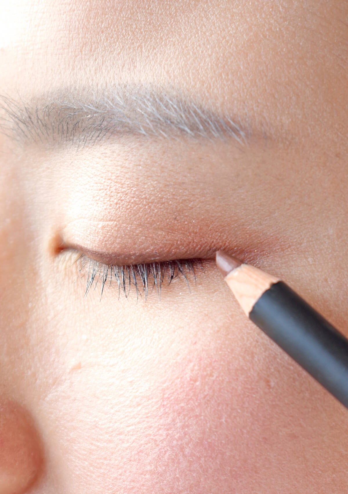 geschlossenes Auge, welches über dem Wimpernkranz einen braunen Strich gezeichnet hat. Der braune Augenkonturenstift ist am Ende des Auges zu sehen