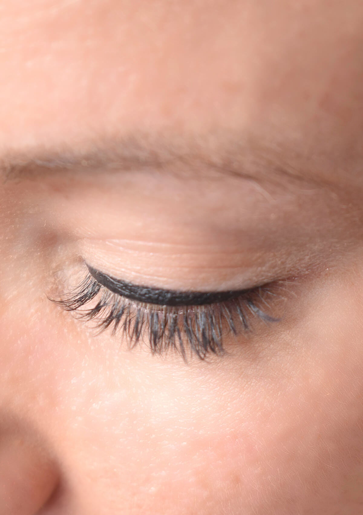 geschlossenes Auge, welches über dem Wimpernkranz einen schwarzen Strich gezeichnet hat.