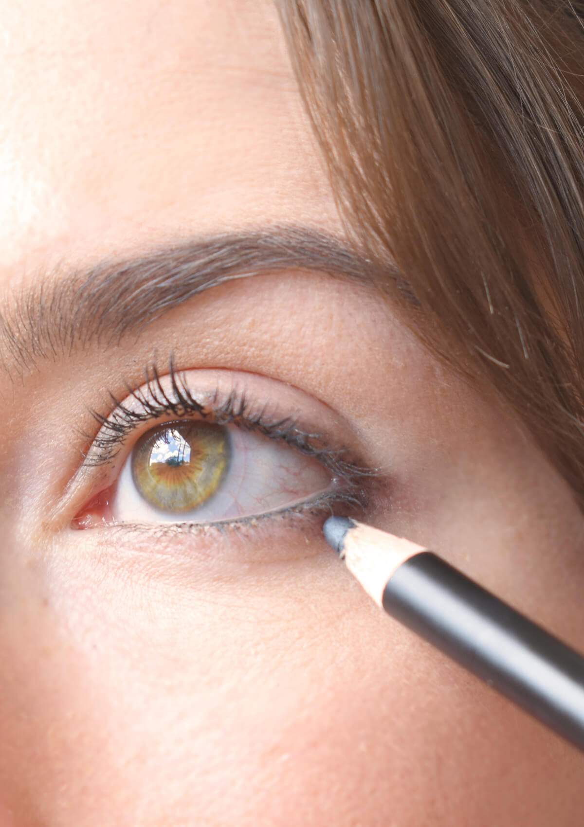 offenes Auge, welches am unteren Wimpernkranz einen grauen Strich gezeichnet hat. Der graue Augenkonturenstift ist am Ende des Auges zu sehen