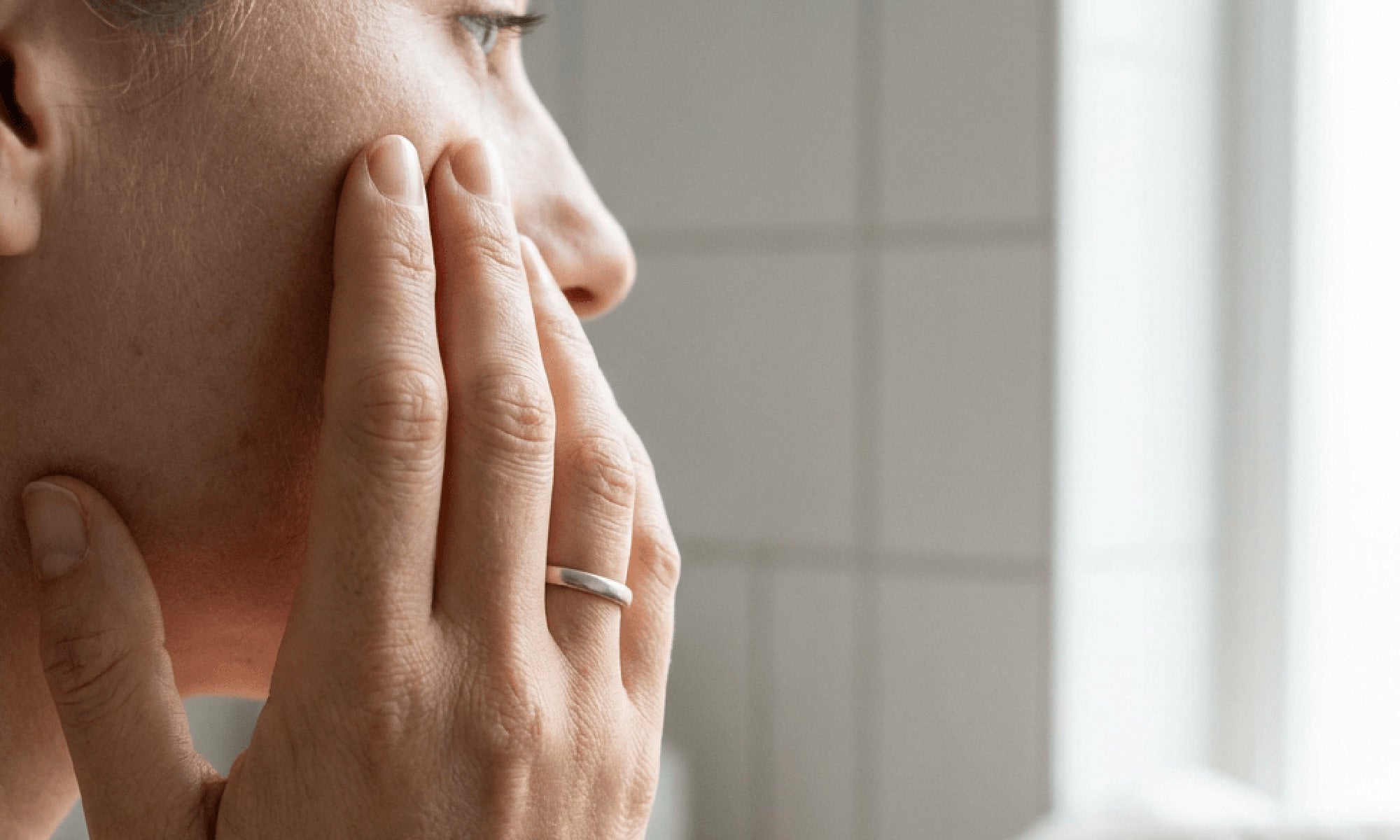 Frau im Badezimmer hält Hand an die Wange und schaut nachdenklich